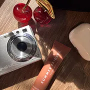 A flat lay from my desk: a vintage camera, a cherry ornament and a lip balm in afternoon sun
