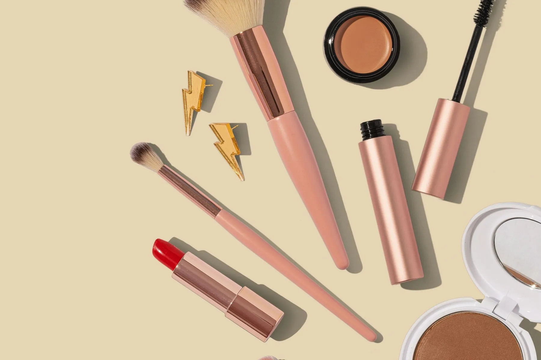 Makeup brushes, a lipstick and a compact laid out on a cream background