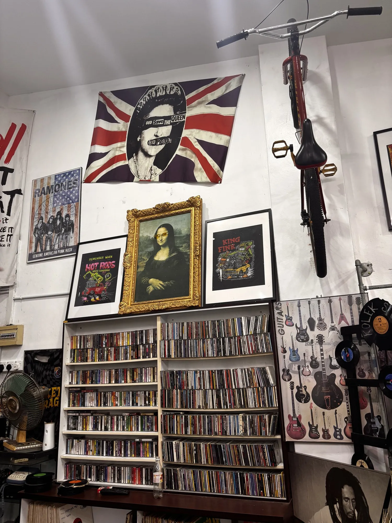 The wall of an independent music shop: shelves of CDs, framed posters and a bike hung up high