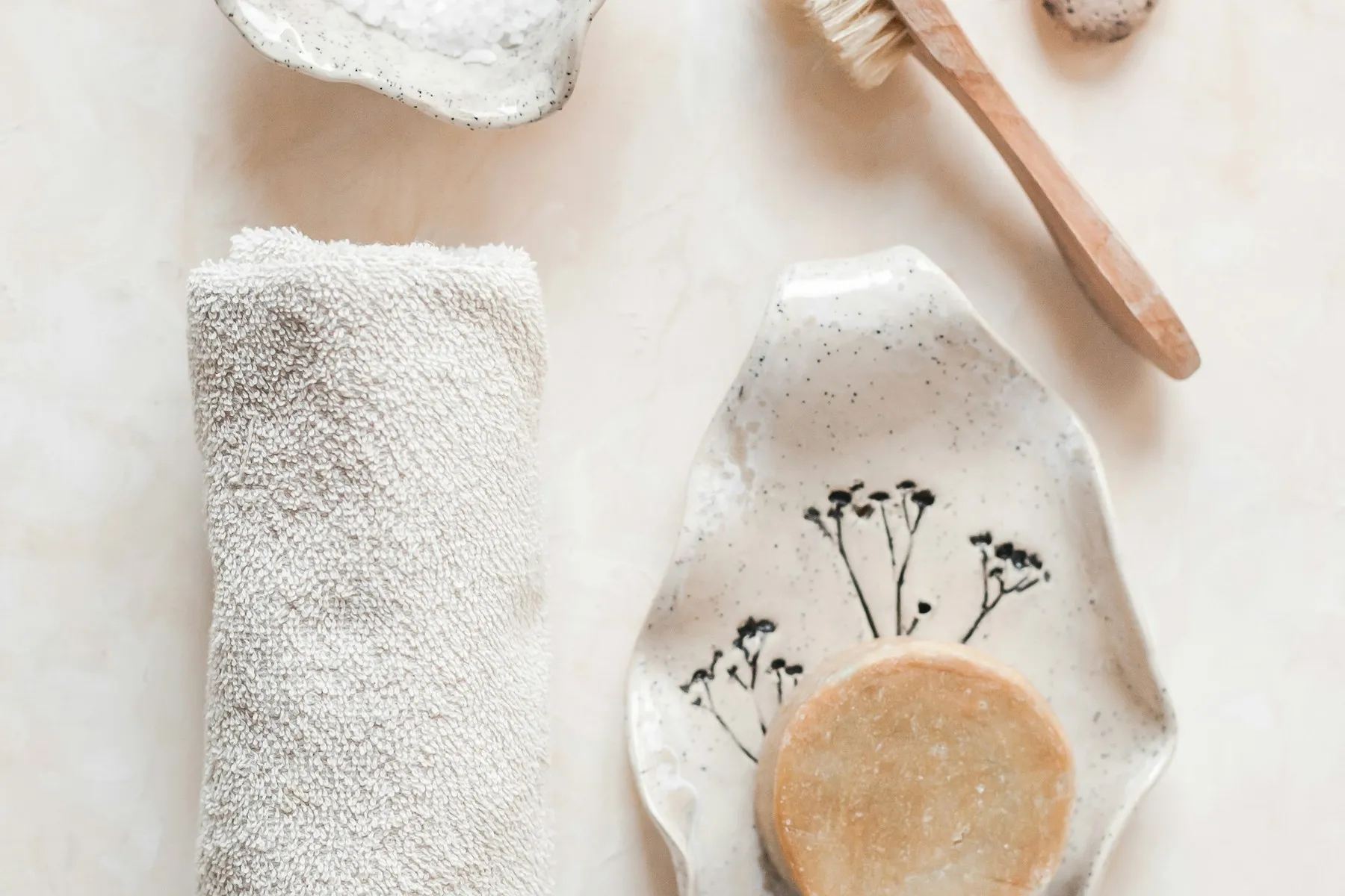 A rolled white towel, a bath brush and a soap bar on a ceramic dish
