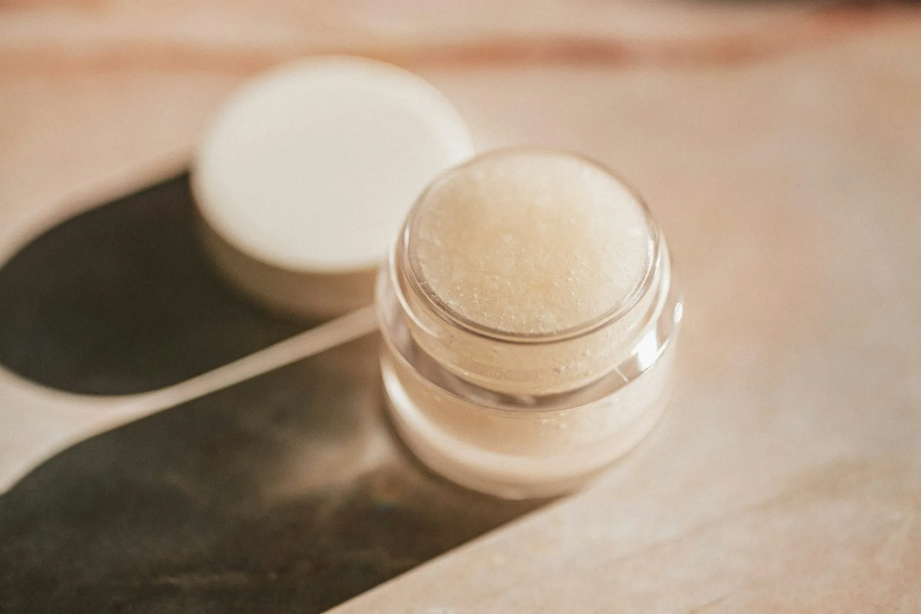 A small open jar of lip balm on a stone surface in soft light
