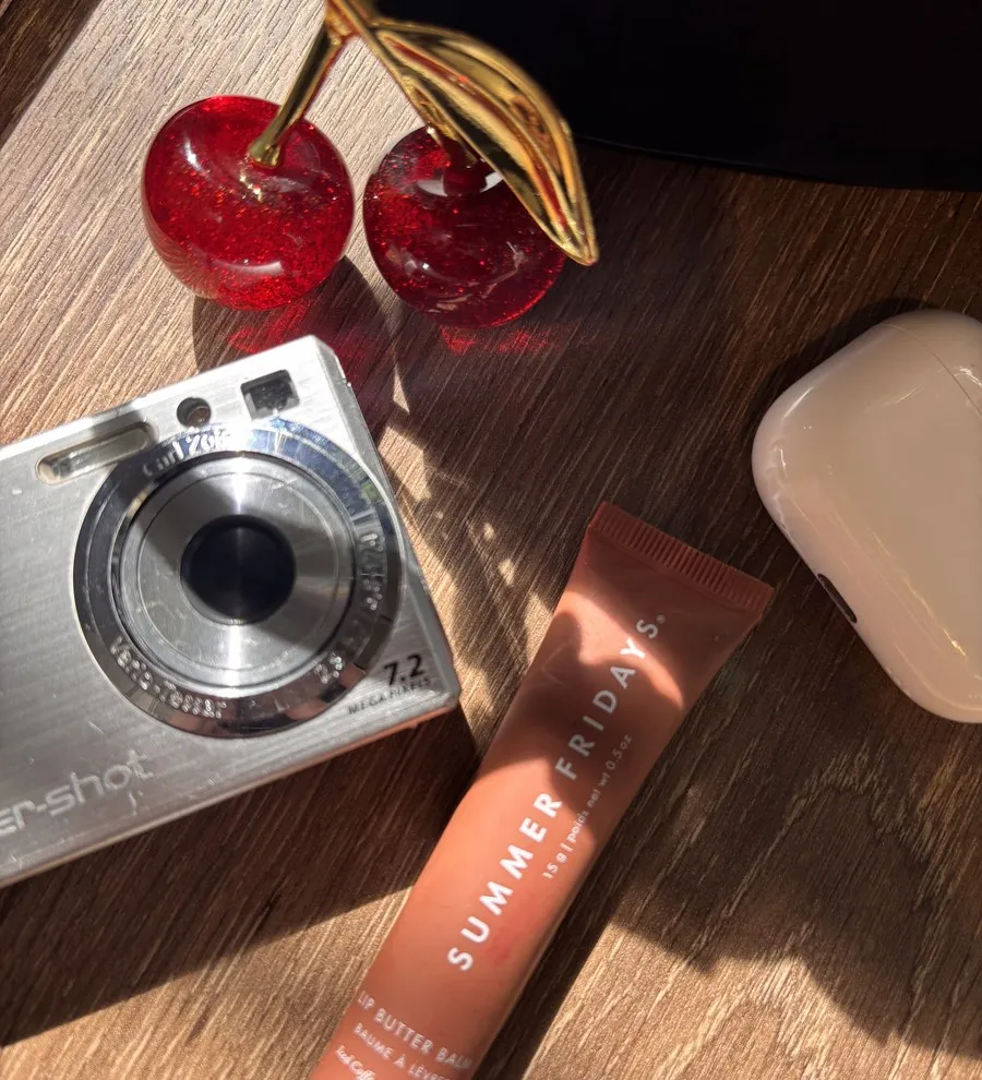 A flat lay from my desk: a vintage camera, a cherry ornament and a lip balm in afternoon sun